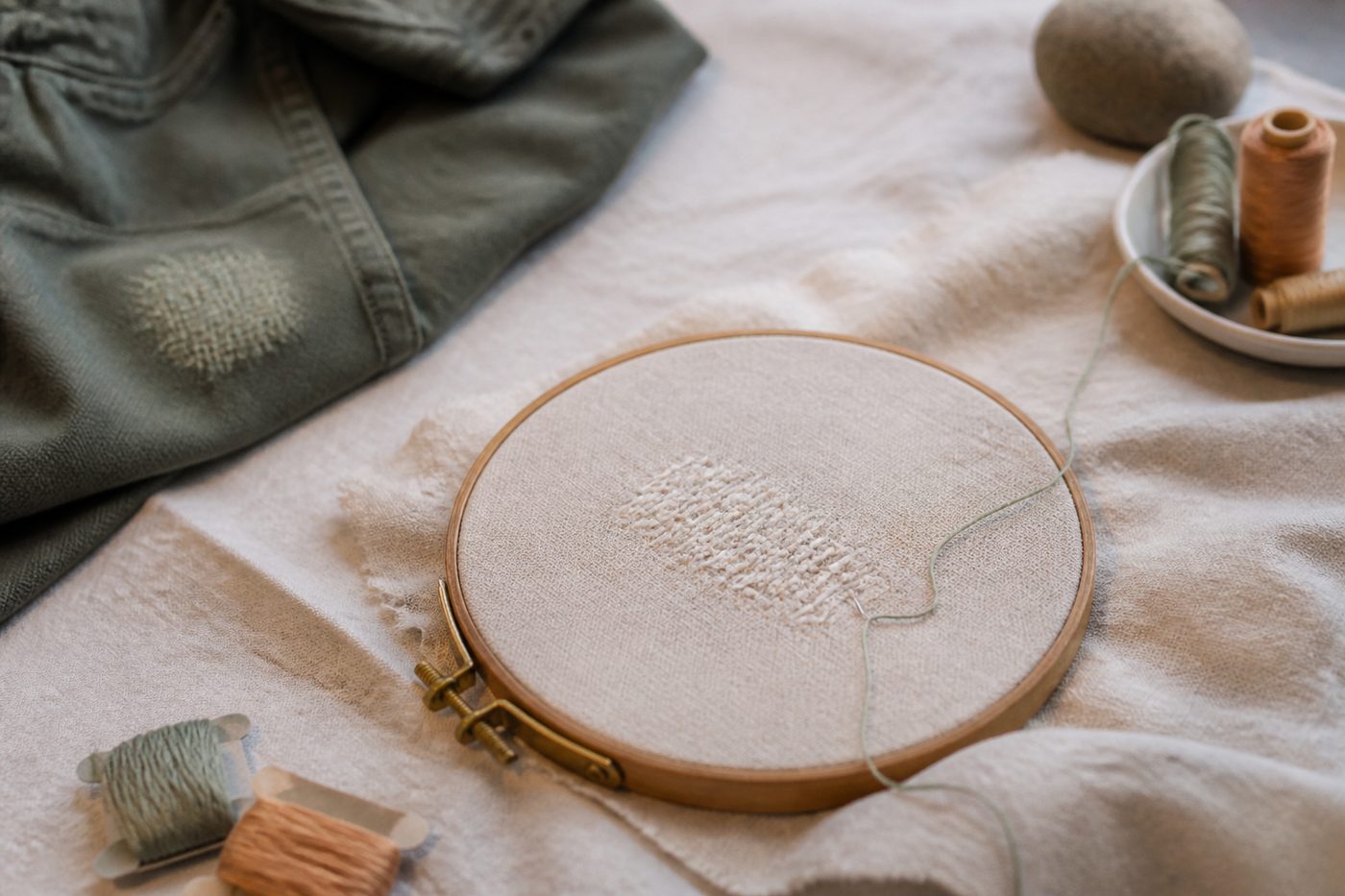 Tambour à broder en bois posé sur une toile écrue, entouré d'écheveaux de fils colorés et d'une paire de petits ciseaux