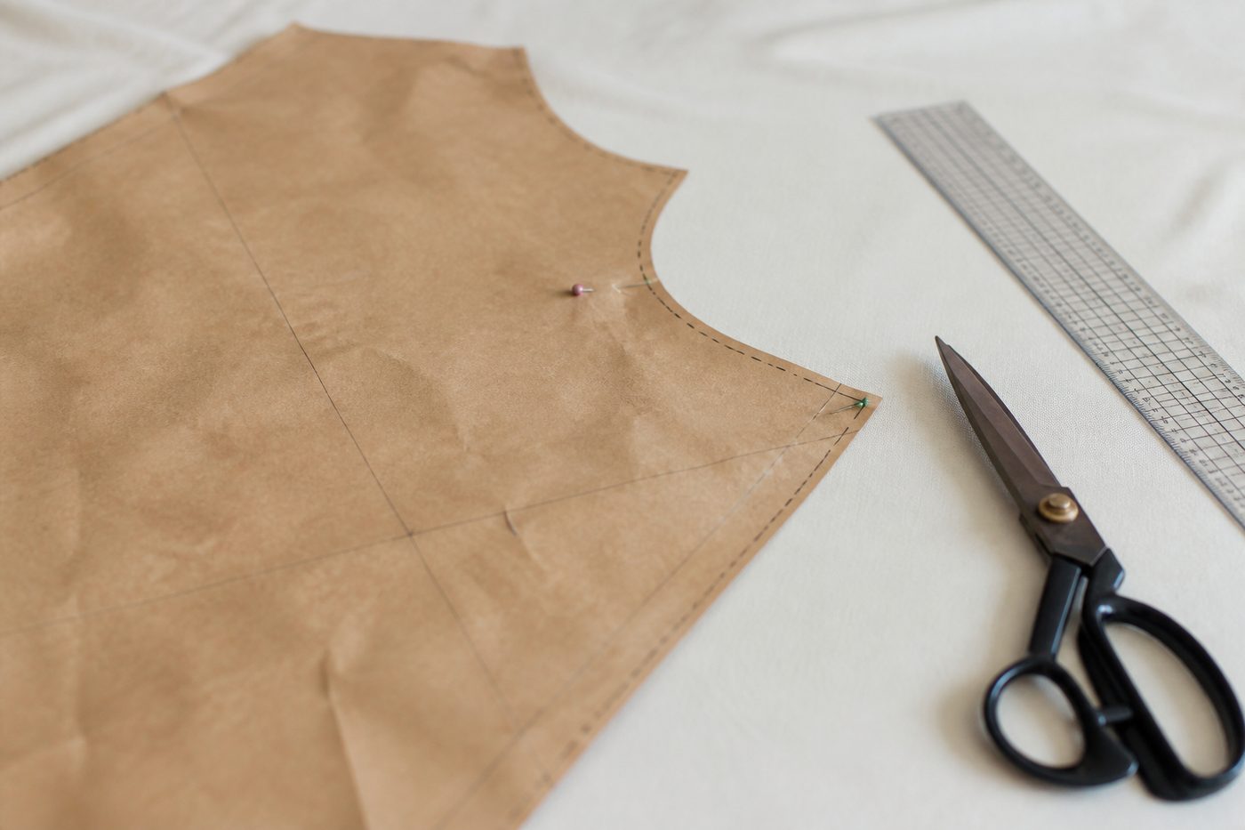 Sur une table en bois clair près d'une fenêtre, un carré de lin é cru tendu sur un cadre, un calque posé dessus avec un motif de bambou au crayon, une bobine de fil noir et une aiguille plantée dans le tissu, lumière douce de fin d'après-midi, cadrage serré à hauteur de table.